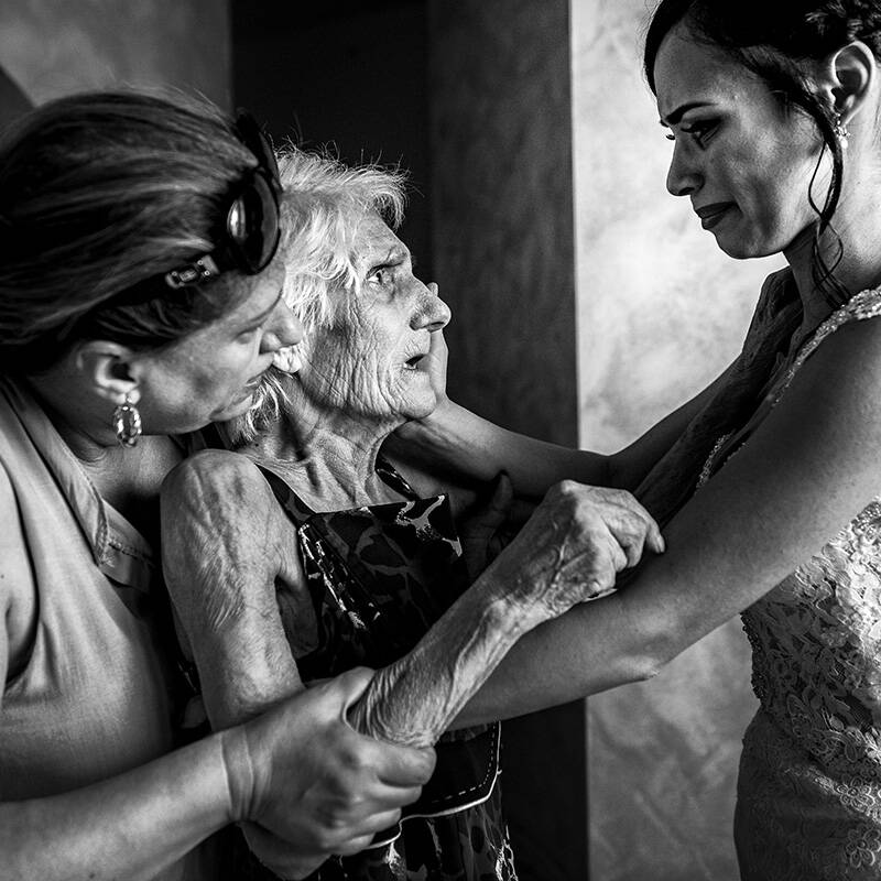 Un'intensa scena di famiglia durante un matrimonio: la sposa con la nonna e un parente in un momento di forte emozione, catturato in bianco e nero da Pasquale Minniti.